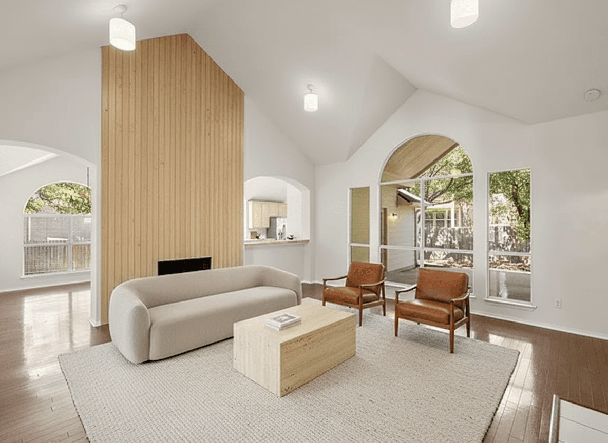 A bright living room featuring a white oak paneled fireplace wall, a cream boucle sofa, two cognac leather lounge chairs, and a travertine c